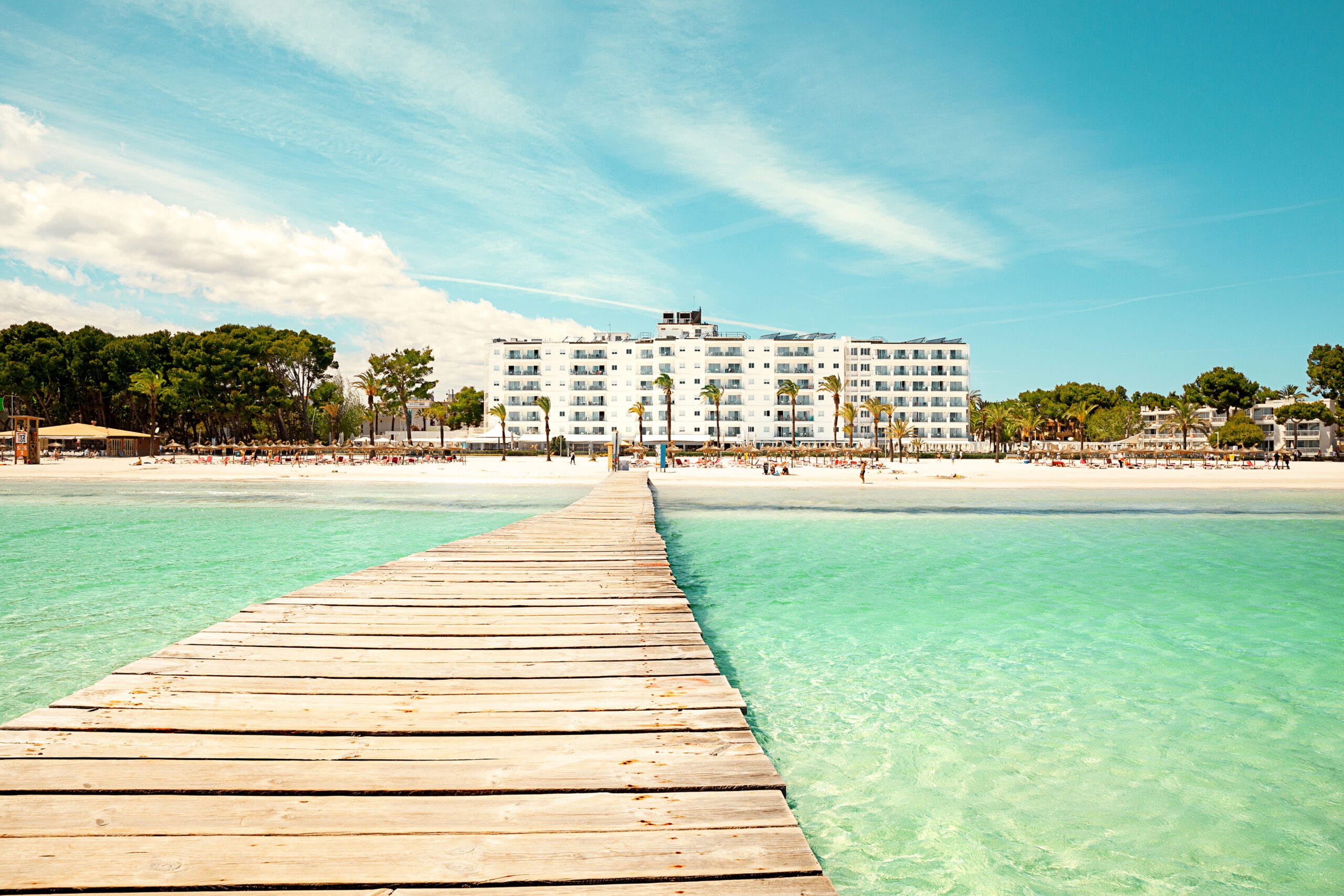 Brygga mot hotell och strand vid turkost vatten