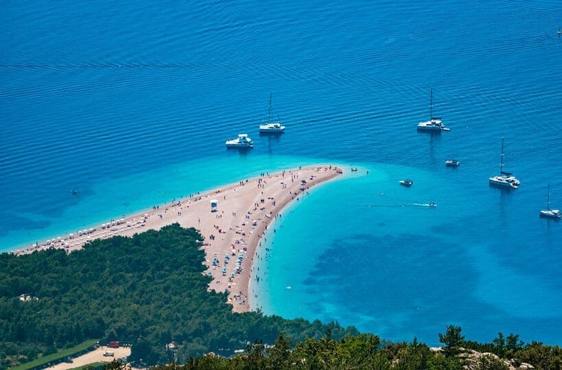 Strand med turkost vatten och båtar.